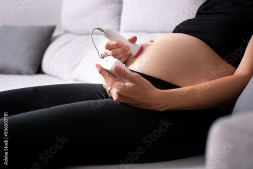 Tableau sur toile Pregnant woman with a fetal doppler listening to the baby's heart sitting on the
