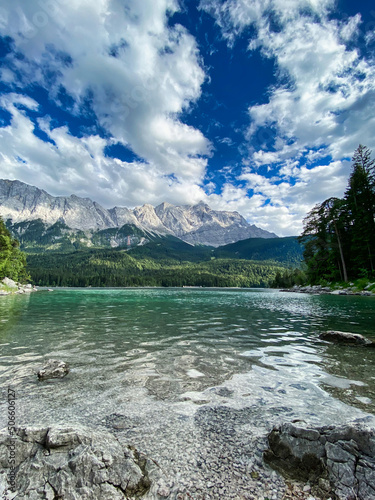 Beautiful shot of a perfect clear mountain lake close to Zugspitze, Germany with turquoise water and the mountain range with dramatic clouds in the background on a summer vacation day. 