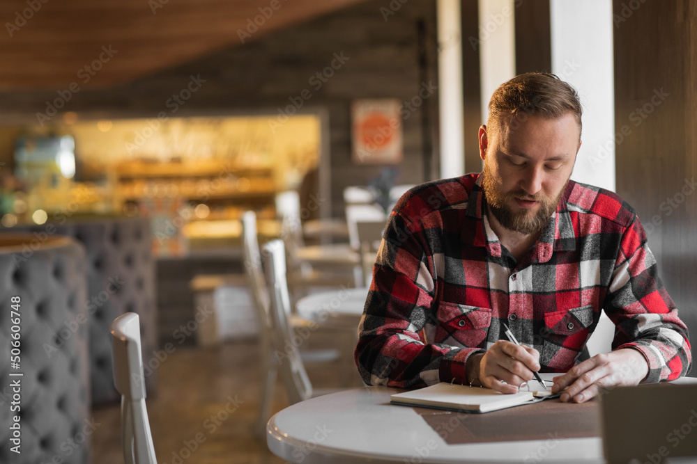 Hardworking white man writing down info at notepad, getting ready for test at cafe. working day start. American guy studying at coffee shop, finding data for his coursework