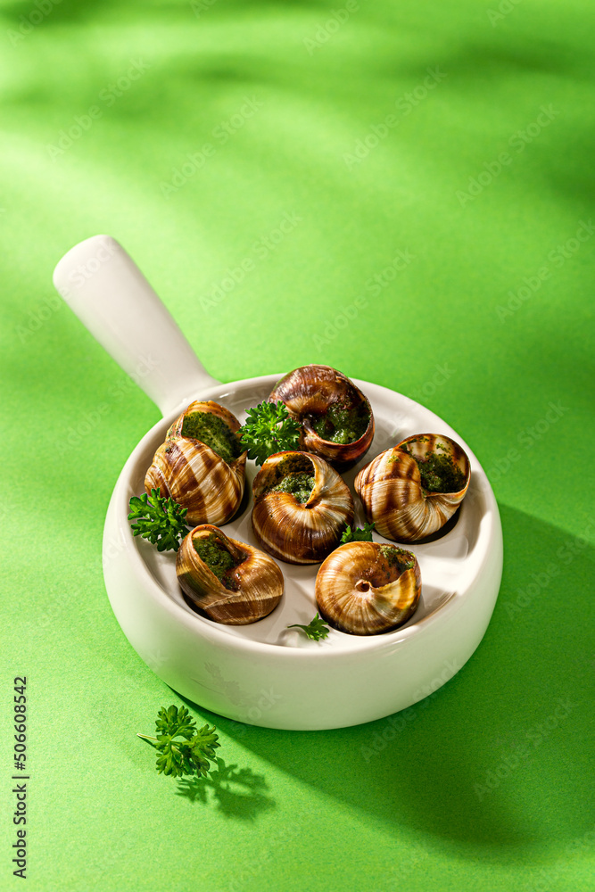 Bourgogne Escargot Snails with garlic herbs butter in ceramics pan on green background with copy space. High view shot with gobo shadows