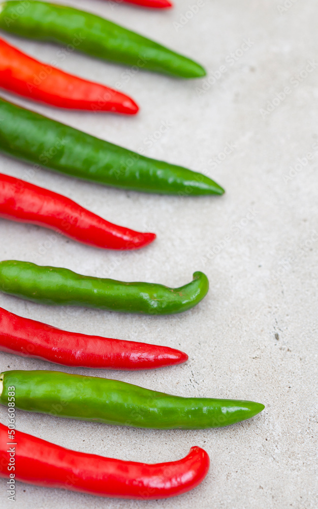 bright small red and green chilies on light grey with copy space