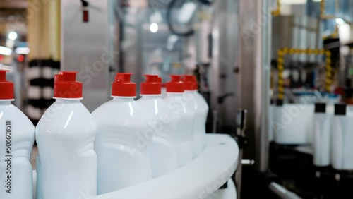 White bottles with red caps ride on a conveyor belt in a factory