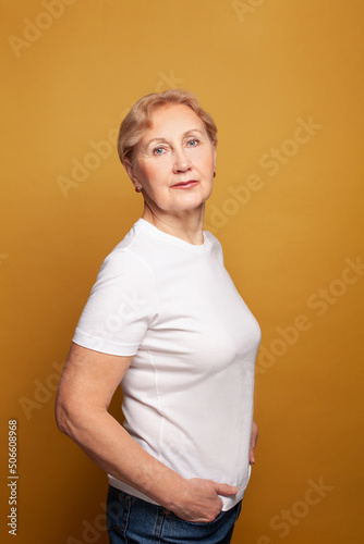 Blonde model senior woman in white t-shirt standing on bright yellow studio wall background