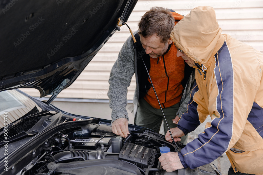 Auto mechanics, Caucasian White mans, working in a car repair shop. Installing the new battery under the hood. Auto mechanics, Caucasian White mans, working in a car repair shop. Installing the new battery under the hood.