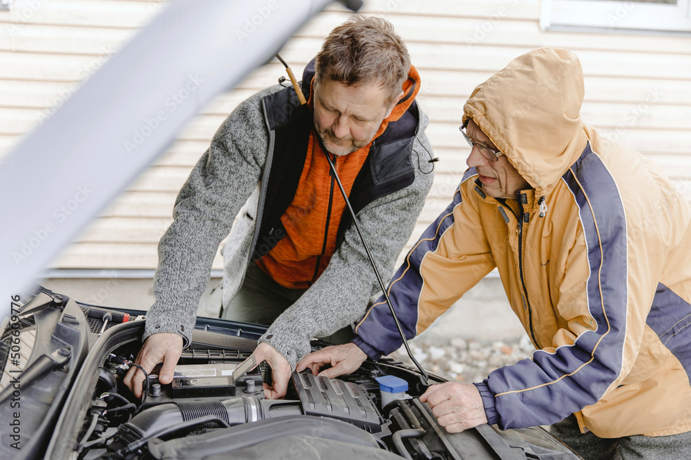 Auto mechanics, Caucasian White mans, working in a car repair shop. Installing the new battery under the hood. Auto mechanics, Caucasian White mans, working in a car repair shop. Installing the new battery under the hood.