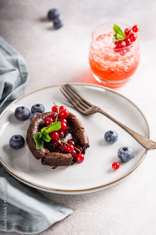 High angle view of warm chocolate pudding lava cake with fondant centre, red currants, bleuberry and mint leaves on gray background High angle view of warm chocolate pudding lava cake with fondant centre, red currants, bleuberry and mint leaves on gray background