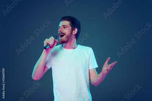Handsome man in white t-shirt singing at microphone isolated on dark blue studio background, Concept of human emotions, facial expression, sales, ad, fashion and beauty