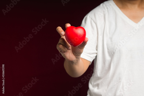Fototapeta Naklejka Na Ścianę i Meble -  Close-up of hand holding a red heart shape while standing on a red background