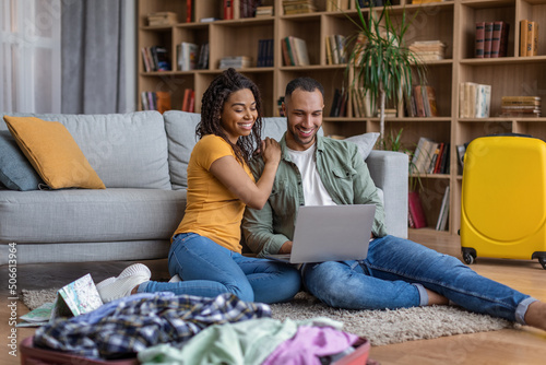 Fotografi Excited black couple with laptop and travel suitcases planning holiday trip, boo