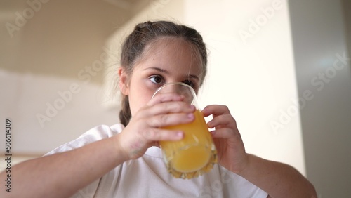 girl child drinking juice. happy family a healthy eating kid dream concept. daughter girl drinking yellow juice from a glass cup in the kitchen. indoors child drinking fruit juice