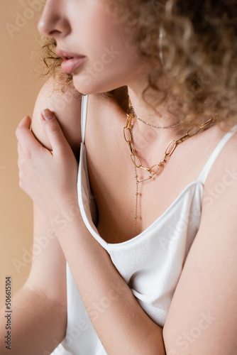 Cropped view of woman in white top and necklaces isolated on beige.