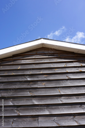 top of wooden barn. Wood cabin roof side view under blue sky. Rural out building. 