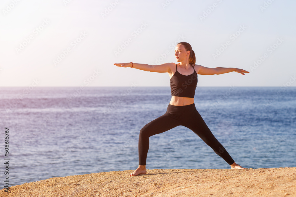 Young fitness woman performing warrior yoga pose at the beach in the morning. Young fitness woman performing warrior yoga pose at the beach in the morning.