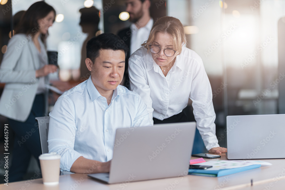 Two diverse business people focused while working on a laptop together at boardroom table in office. Two diverse business people focused while working on a laptop together at boardroom table in office.