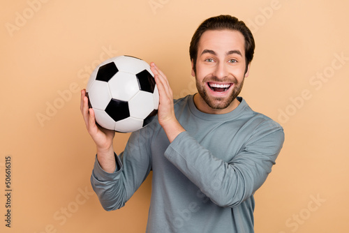 Portrait of satisfied glad man arms hold football toothy smile look camera isolated on beige color background