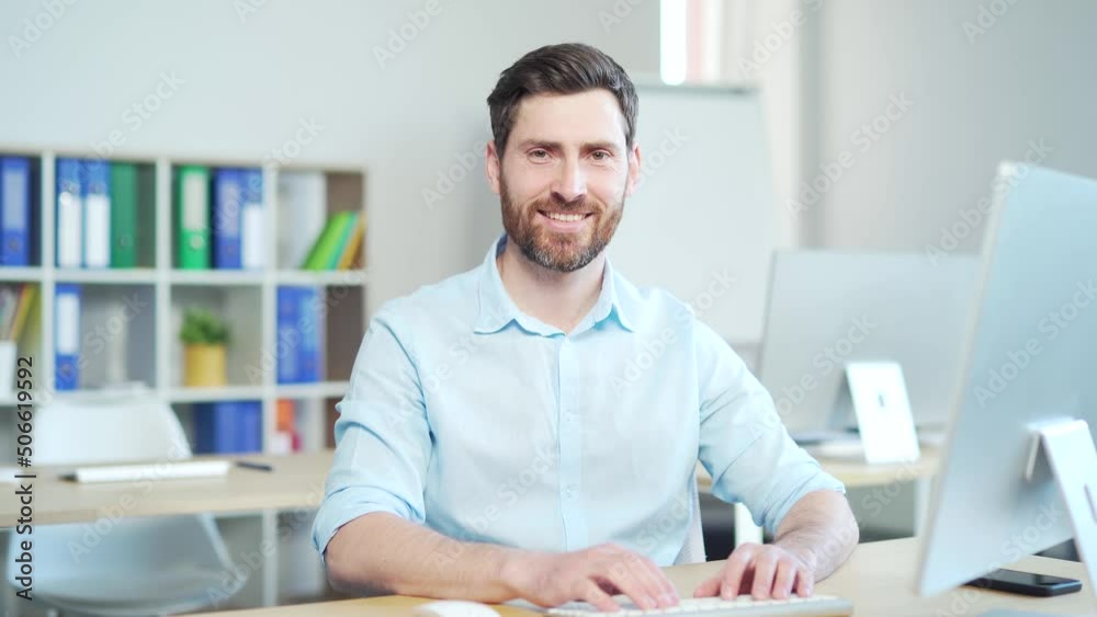Close-up portrait of a happy bearded handsome man at workplace at computer desk in office. Business male employee entrepreneur or manager sitting and looking at camera smiling. confident men at work. Close-up portrait of a happy bearded handsome man at workplace at computer desk in office. Business male employee entrepreneur or manager sitting and looking at camera smiling. confident men at work.