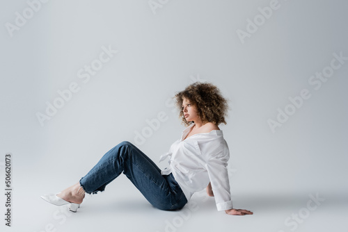 Stylish model in jeans sitting on white background.