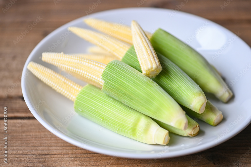 Fresh young baby corn for cooking health food, Close up raw organic baby corn on wooden background, Baby corn on white plate. Fresh young baby corn for cooking health food, Close up raw organic baby corn on wooden background, Baby corn on white plate.