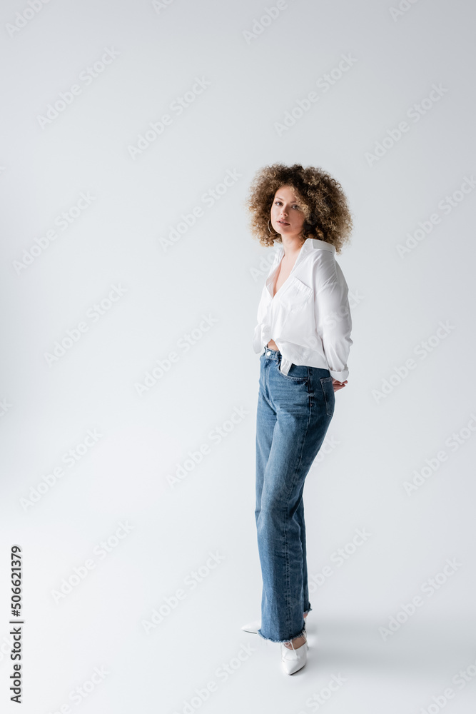 Curly woman in blouse and jeans looking at camera on white background. Curly woman in blouse and jeans looking at camera on white background.