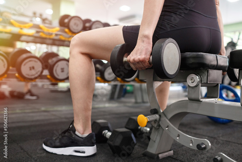 Adult athletic woman in black sportswear performs strength training in the gym. Girl lifts heavy weights on the background of sports equipment. Theme of health, sports lifestyle.