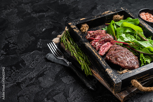 BBQ roasted flank steak in wooden tray with vegetable salad. Black background. Top view. Copy space