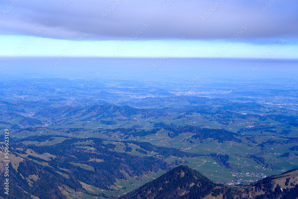 Aerial view with Mountains and midland in the background seen from Säntis peak at Alpstein Mountains on a sunny spring day. Photo taken April 19th, 2022, Säntis, Switzerland.