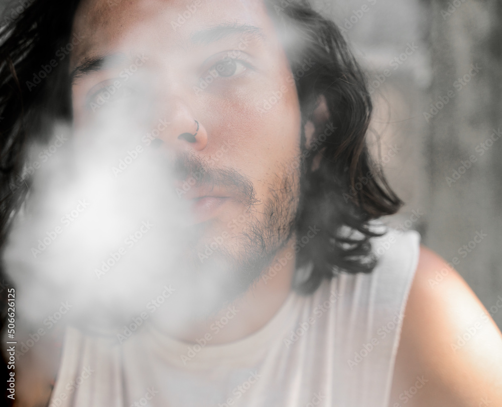 Attractive young dark haired man puffing out smoke from a cigarette, head shot