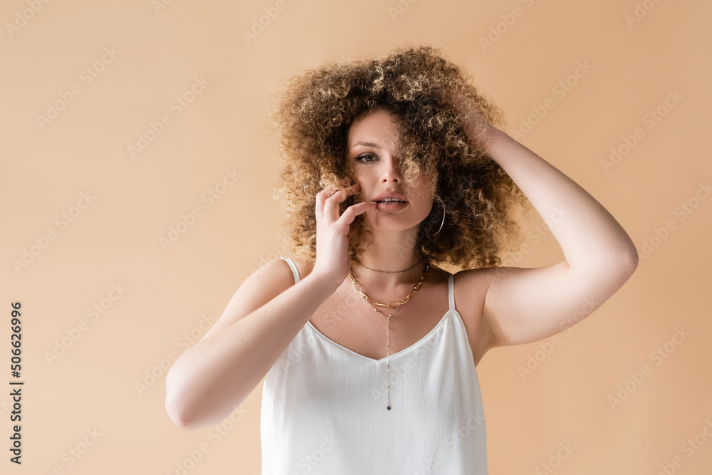 Young woman in white top touching curly hair isolated on beige. Young woman in white top touching curly hair isolated on beige.