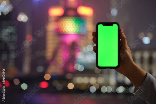 hand showing green screen phone with blur colorful Shanghai city bokeh background