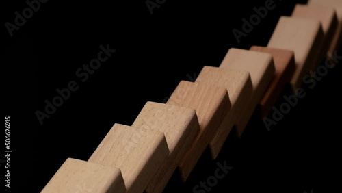 Row of wooden domino falling down against black background. Domino effect. photo