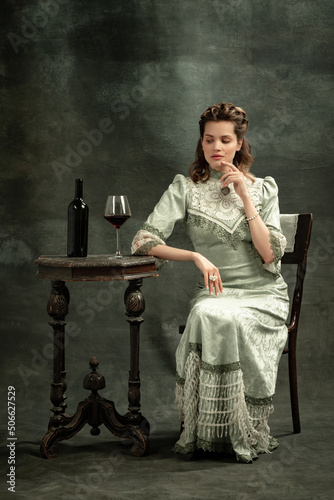 Vintage portrait of young beautiful girl in gray dress of medieval style isolated on dark background. Comparison of eras concept, flemish style. Art, beauty