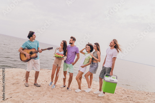 Full body image of young people millennials have fun near seaside lake ocean listen their best friend play guitar