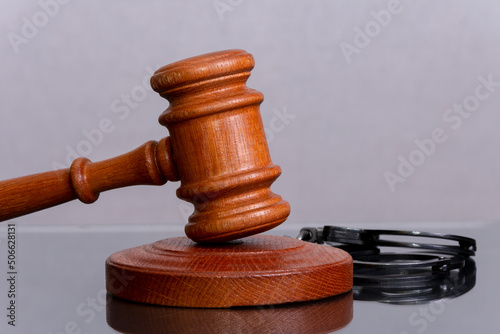 Wooden judge's gavel and police handcuffs on a dark background. Concept: claim and compensation for damages, court session, announcement of the verdict, trial.