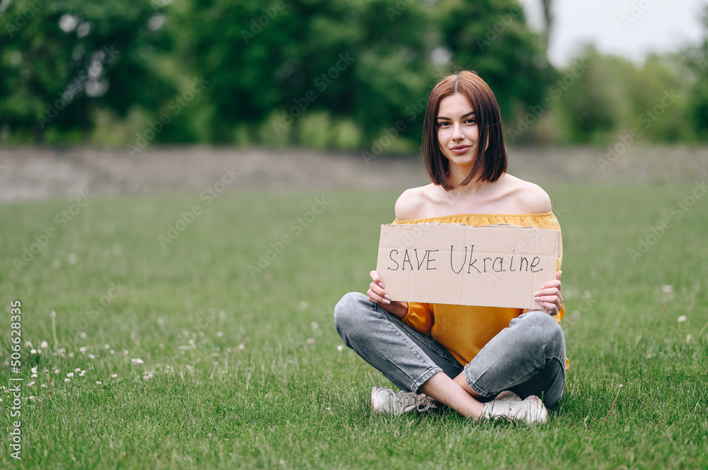 girl Sits on the green grass and asks to save Ukraine. War in the 21st century. girl Sits on the green grass and asks to save Ukraine. War in the 21st century.