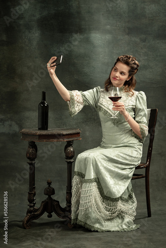 Emotional young beautiful girl, actress in image of medieval person posing isolated on dark background. Comparison of eras concept, flemish style. Art, beauty