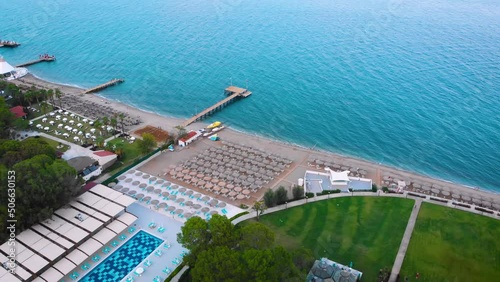 Flight over the beach with sun umbrellas towards the pool in a luxury hotel around of stone mountains on a warm sunny day