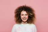 Cheerful curly woman looking at camera isolated on pink.