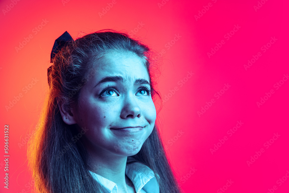 Close-up portrait of young girl, student posing, making funny faces isolated over pink background in neon light Close-up portrait of young girl, student posing, making funny faces isolated over pink background in neon light