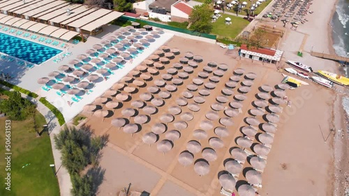 Flight over the beach with sun umbrellas towards the pool in a luxury hotel around of stone mountains on a warm sunny day