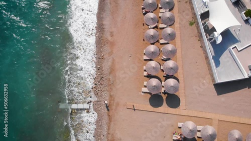 Flight over the beach with sun umbrellas towards the pool in a luxury hotel around of stone mountains on a warm sunny day