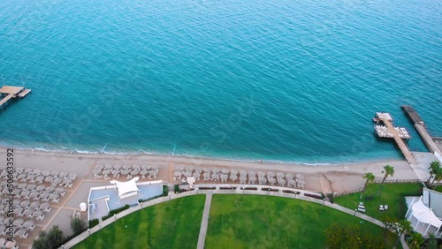 Flight over the beach with sun umbrellas towards the pool in a luxury hotel around of stone mountains on a warm sunny day