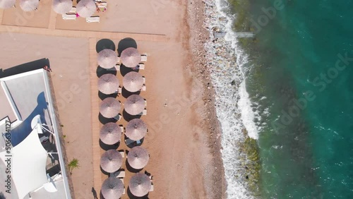 Flight over the beach with sun umbrellas towards the pool in a luxury hotel around of stone mountains on a warm sunny day