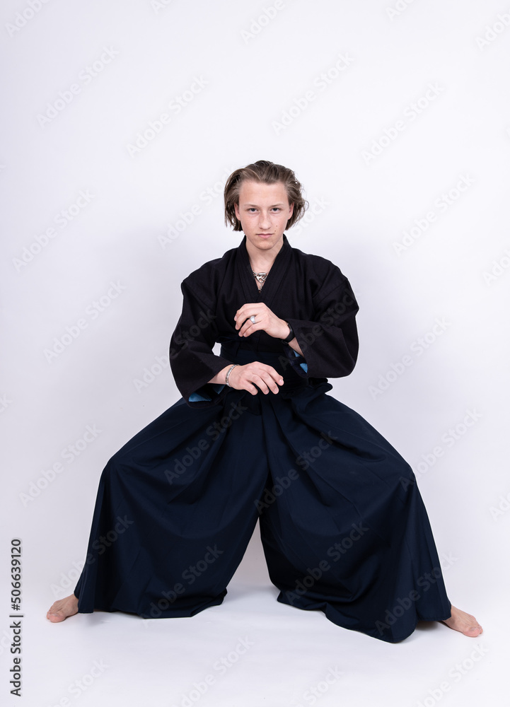 junger mann in traditionellem Kendo Gewand mit gebeugten Knien und gekreuzten Armen