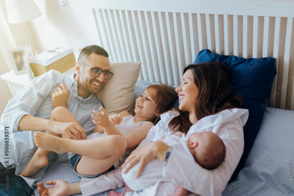 Mother father daughter newborn baby lying in bed smiling Mother father daughter newborn baby lying in bed smiling