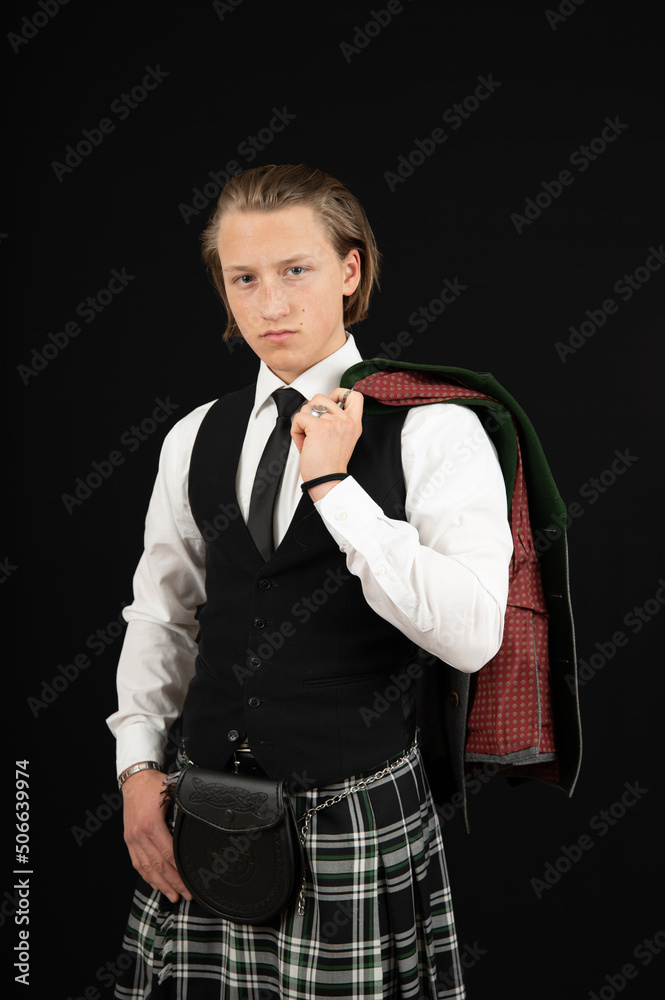 blonder, junger Mann trägt einen Kilt und Trachtenjacke über der Schulter