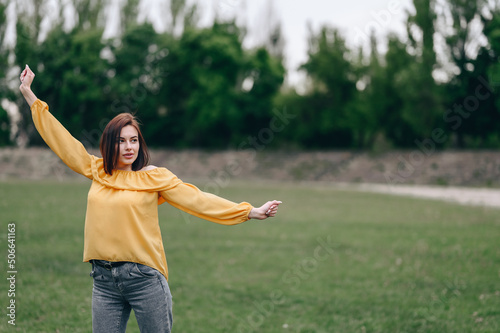 A girl in a yellow blouse spreads her arms to the side and looks into the distance