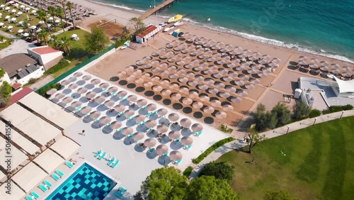 Flight over the beach with sun umbrellas towards the pool in a luxury hotel around of stone mountains on a warm sunny day