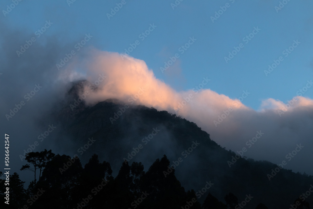 Sea of clouds on top of the mountain, illuminated by sunset light and silhouette of forest, mystery scene, Teresópolis, Rio de Janeiro, Brazil