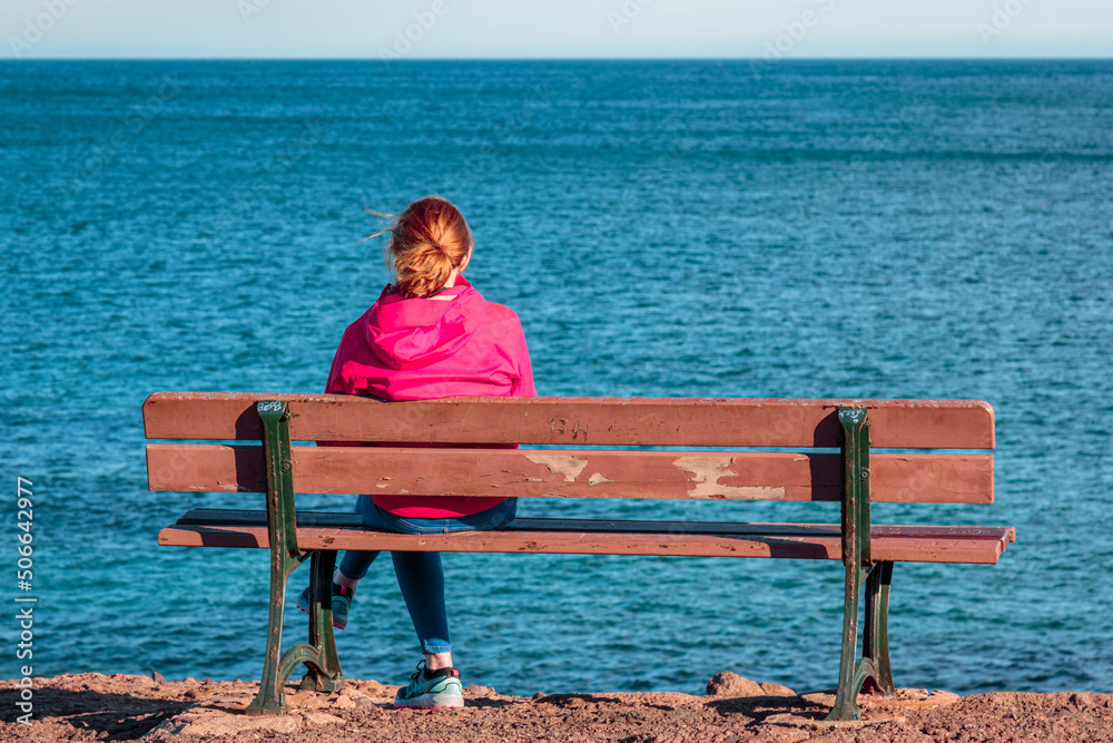one single woman alone sitting on a bench watching the sea horizon