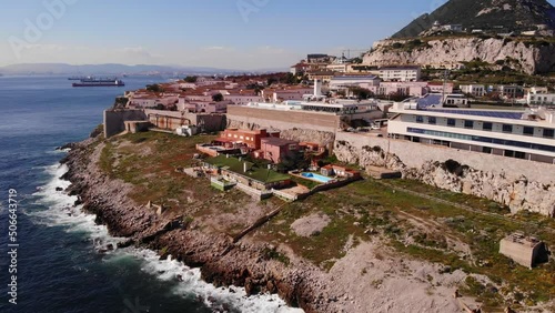 Luxury villa outside city walls of Gibraltar with stunning views at the Algeciras bay as big waves from the Mediterranean splash against the rocks of Europa Point on a sunny day. Drone trucking shot